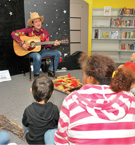 Western party. Youngsters and their families visit the North-East Public Library Oct. 18 for a western themed story time and party. At right, Independence residents Sophan Munger and her three-year-old son Zach try their luck at roping a steer. At left, Northeast resident Scott "Rex" Hobart leads a group in a campfire sing-along. Leslie Collins